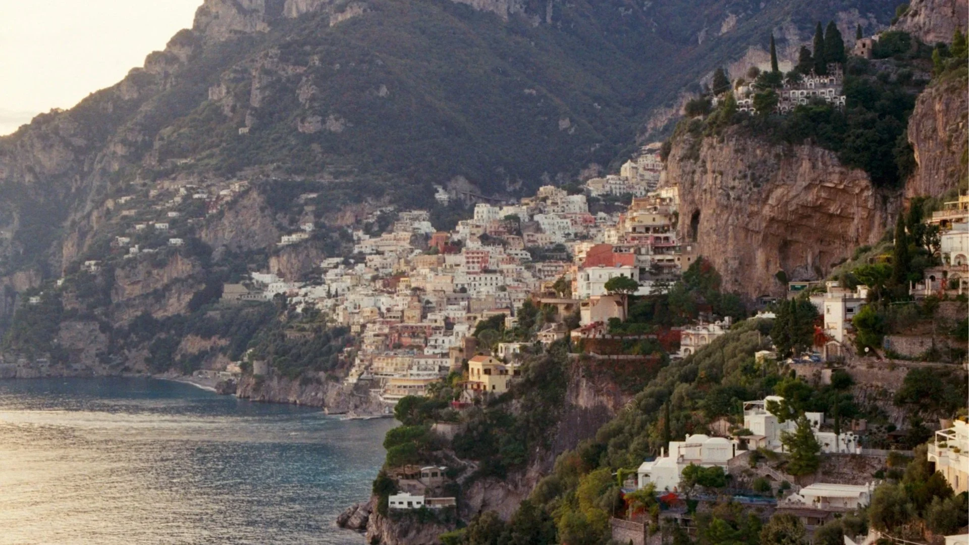A scenic view of colorful buildings perched on a steep cliffside overlooking the ocean in Positano, Italy, during sunset.