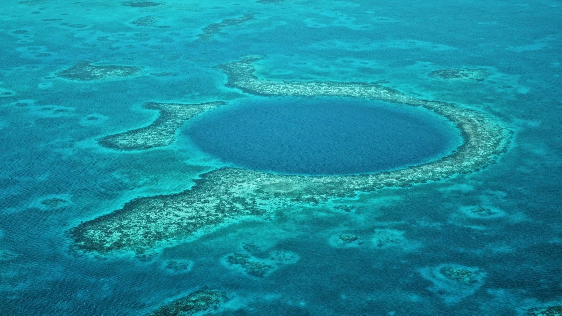 An aerial view of the Great Blue Hole in Belize, a perfectly circular deep blue sinkhole surrounded by turquoise coral reef waters.