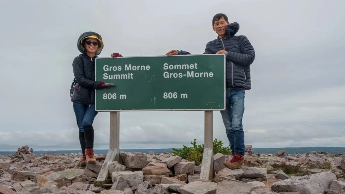 Two hikers posing behind a green park sign for the Gros Morne Summit at an elevation of 806 meters.