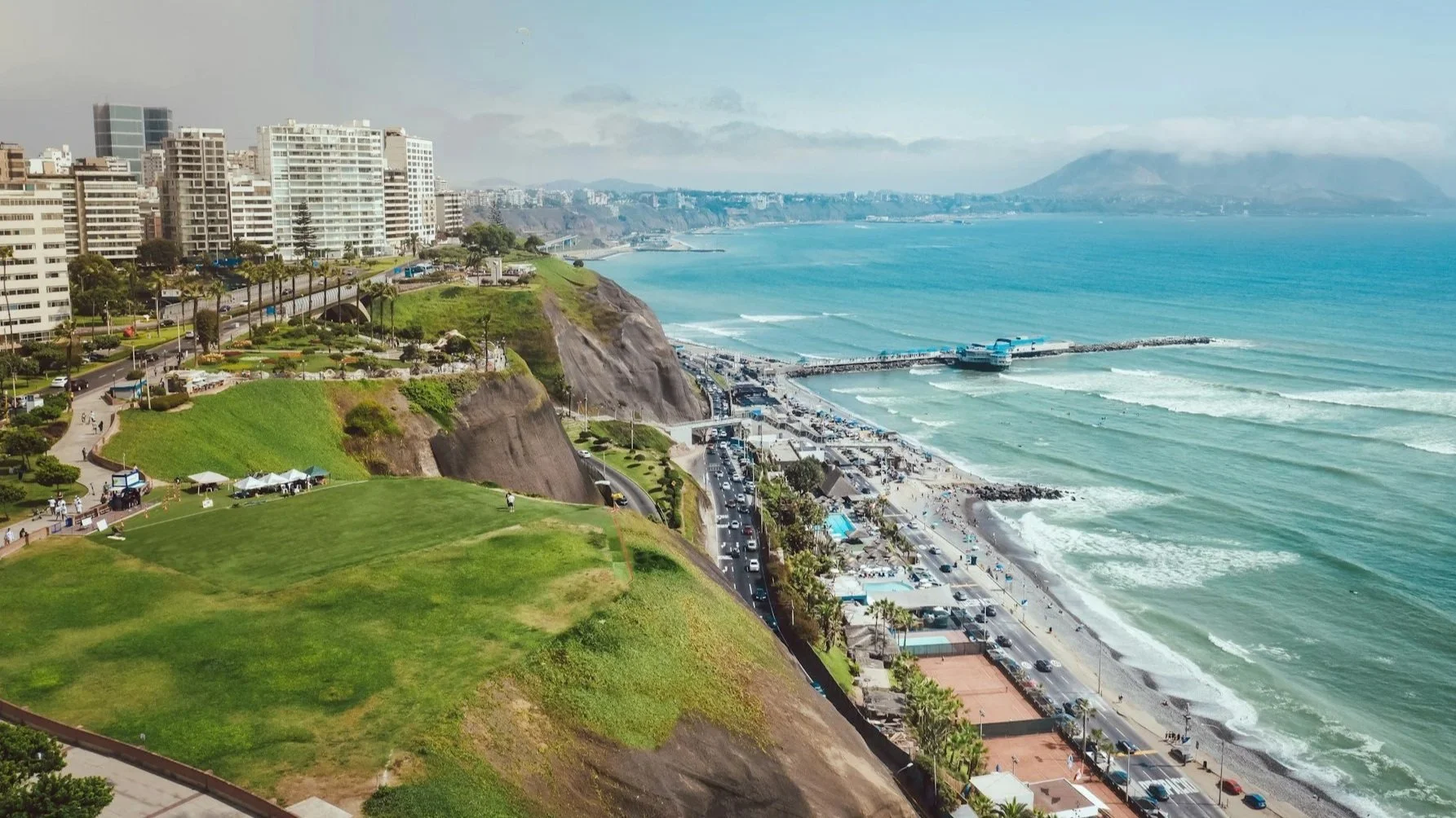 Aerial view of the coastal cliffs and beaches of Miraflores, Lima, with paragliders flying over the Pacific Ocean.