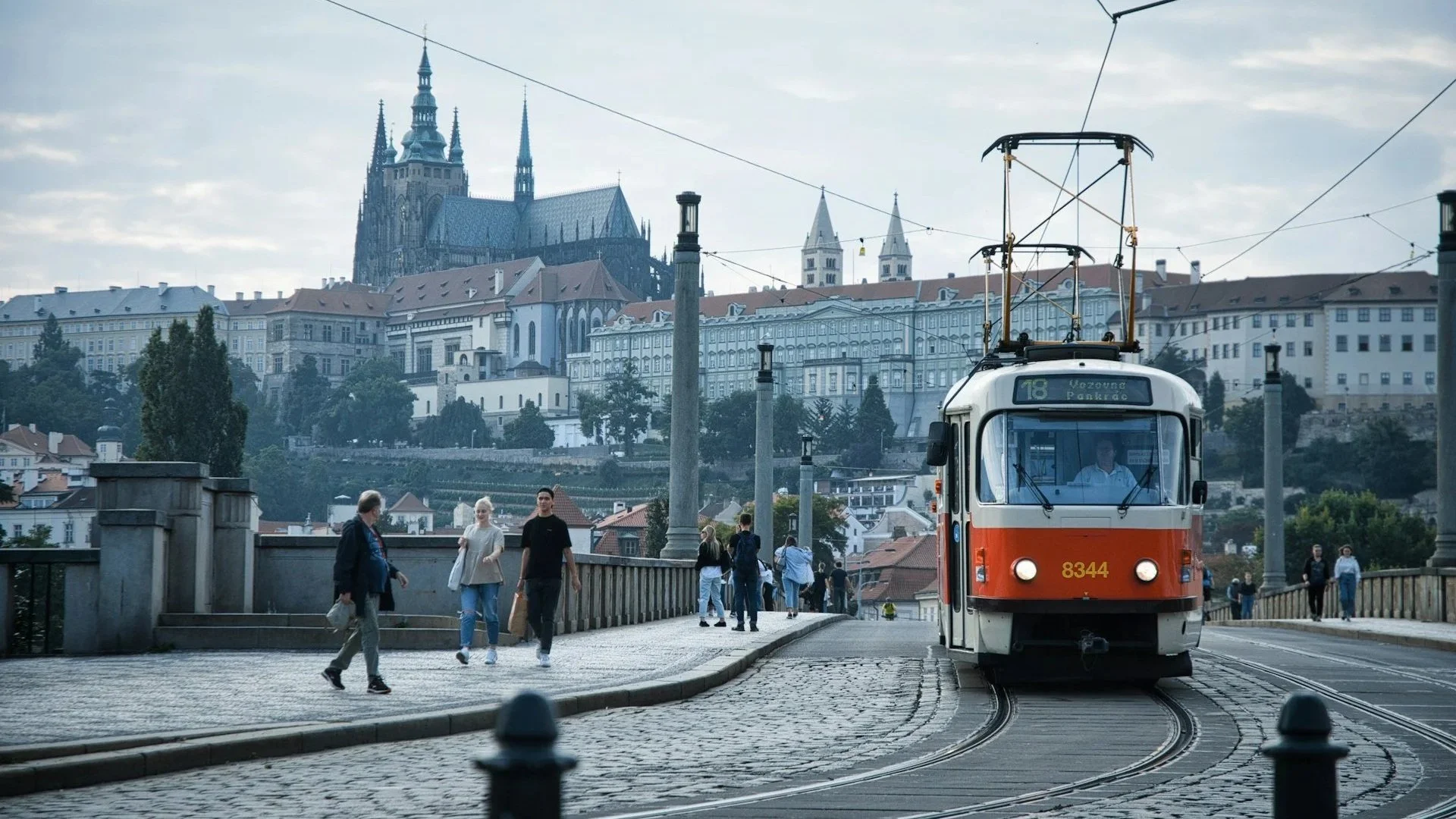 Red and white tram crossing a bridge in Prague, with Prague Castle rising in the background.