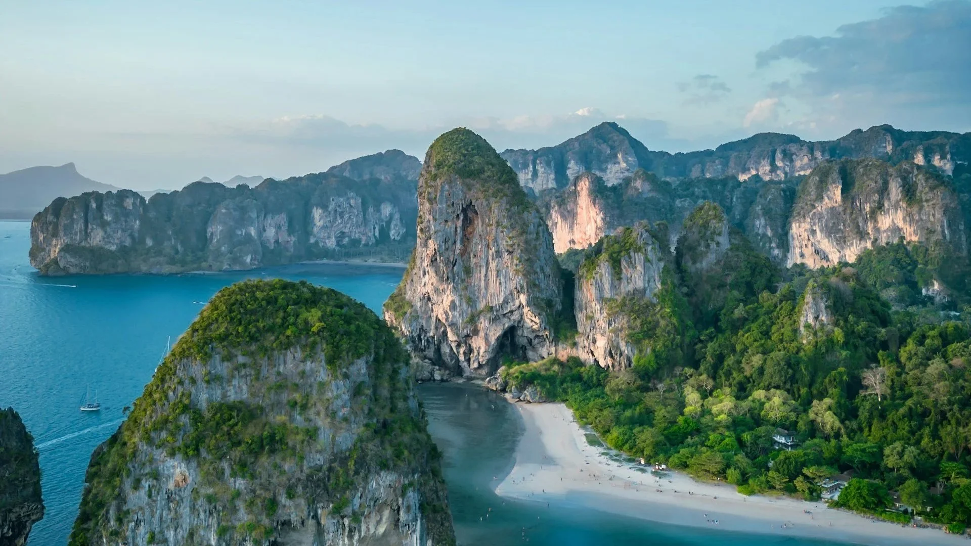 Aerial view of a tropical white sand beach nestled between towering limestone cliffs and turquoise water.