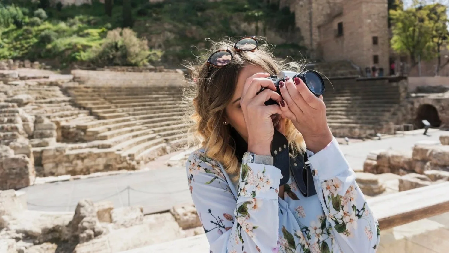 A woman taking a picture of the ancient Roman Theater ruins and the Alcazaba fortress in Málaga, Spain.