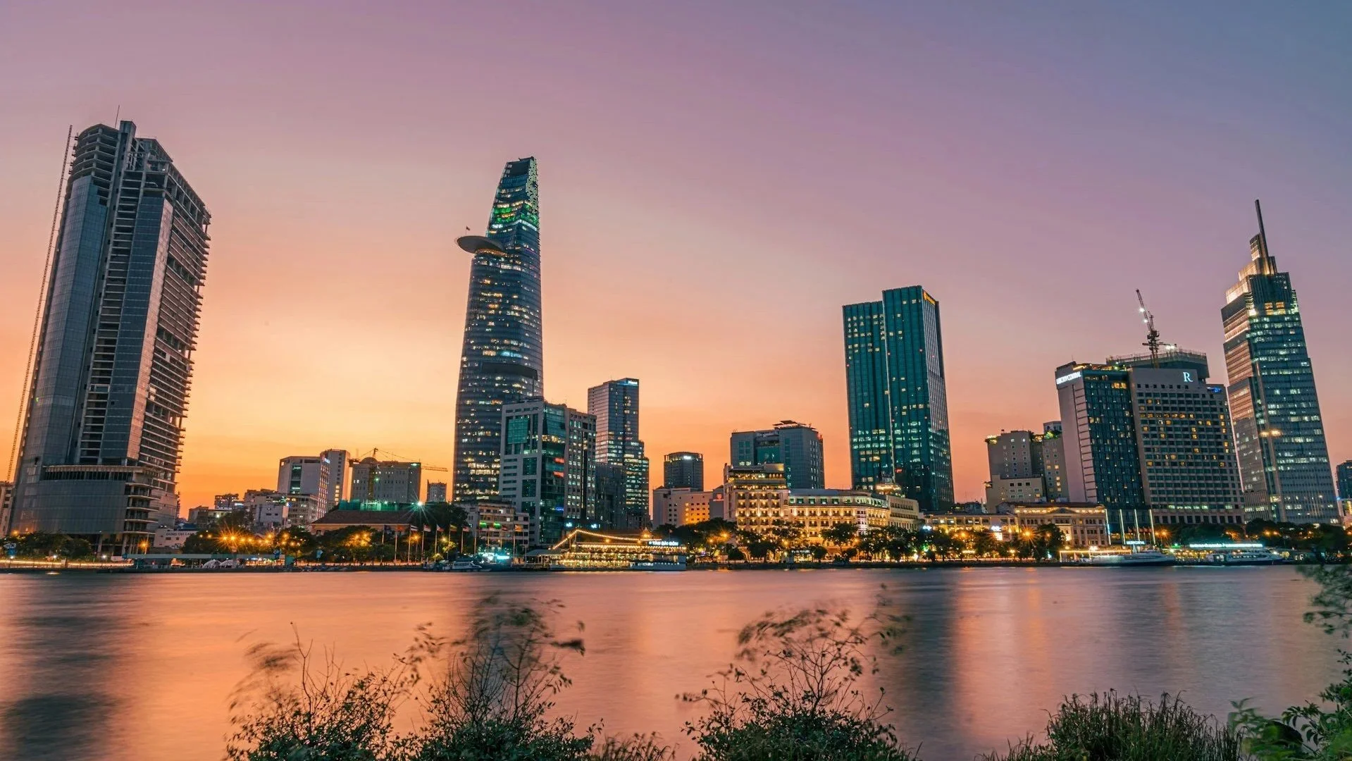 The illuminated skyline of Ho Chi Minh City at dusk, reflected in the Saigon River.