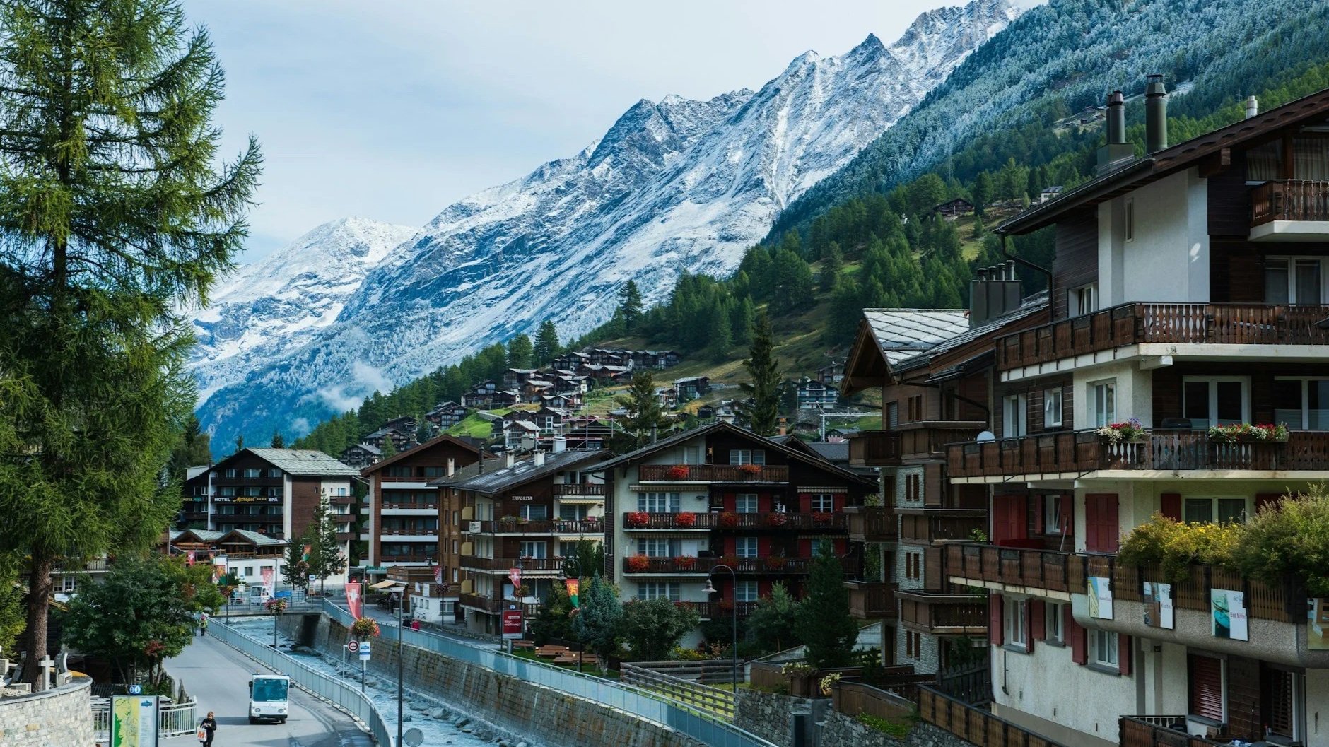A view of Zermatt's wooden chalets and a mountain stream under the towering, snow-dusted peaks of the Swiss Alps.