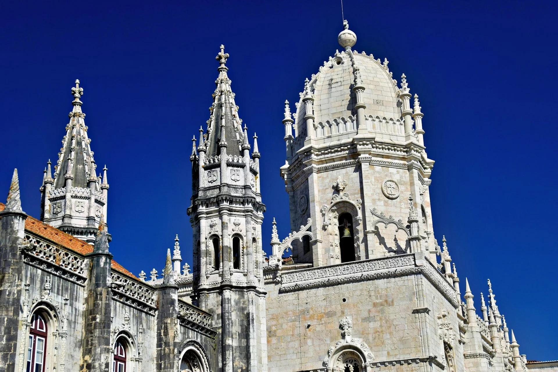 The ornate stone spires and white dome of the Jerónimos Monastery in Lisbon against a clear, deep blue sky.