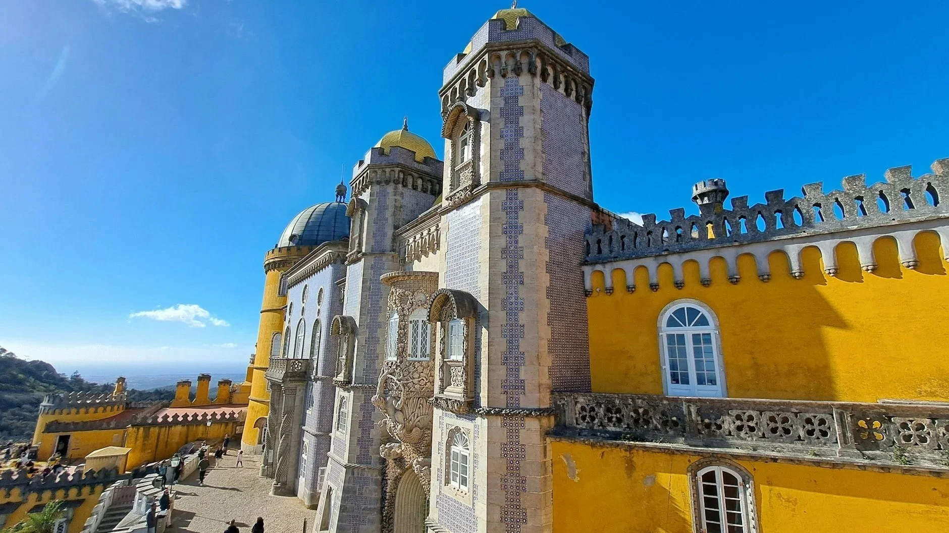 A close-up of the vibrant yellow walls and intricate blue tilework of Pena Palace in Sintra under a clear blue sky.