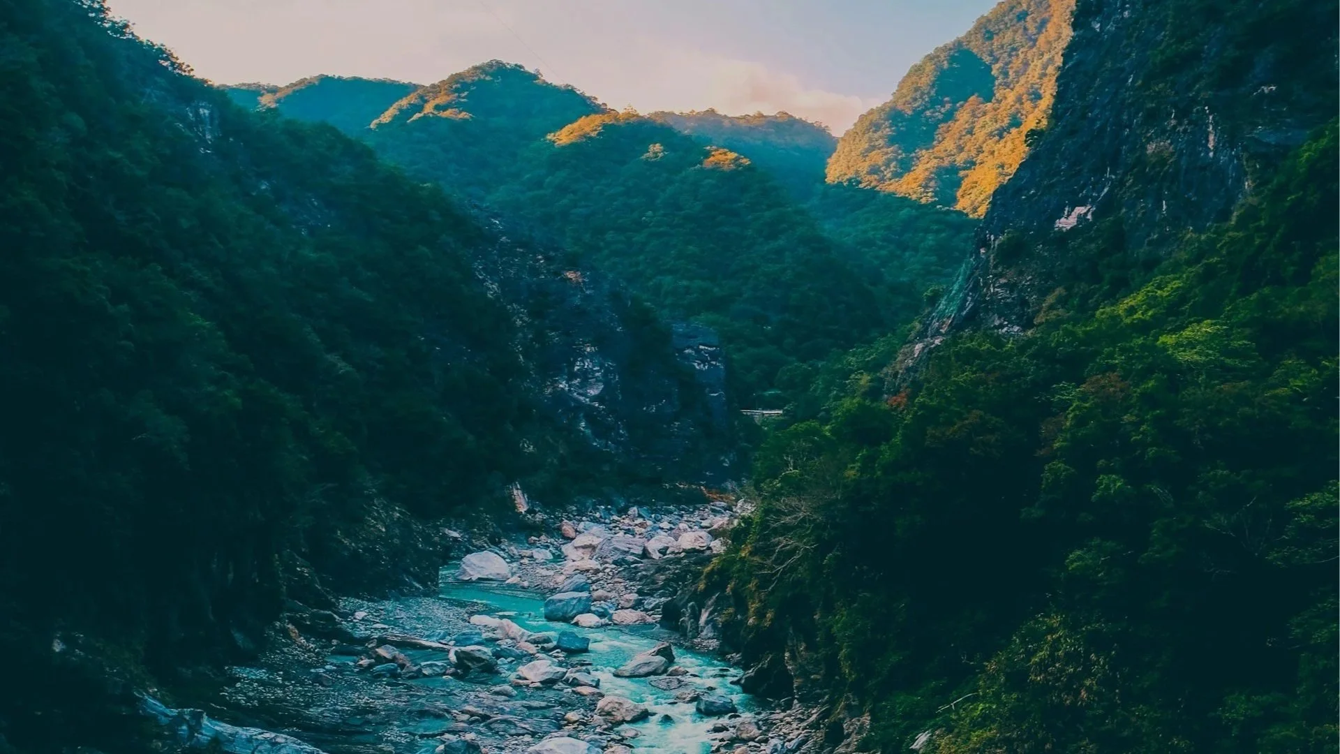 A vibrant turquoise river winding through a steep, rocky mountain gorge surrounded by dense green forests under a clear blue sky.