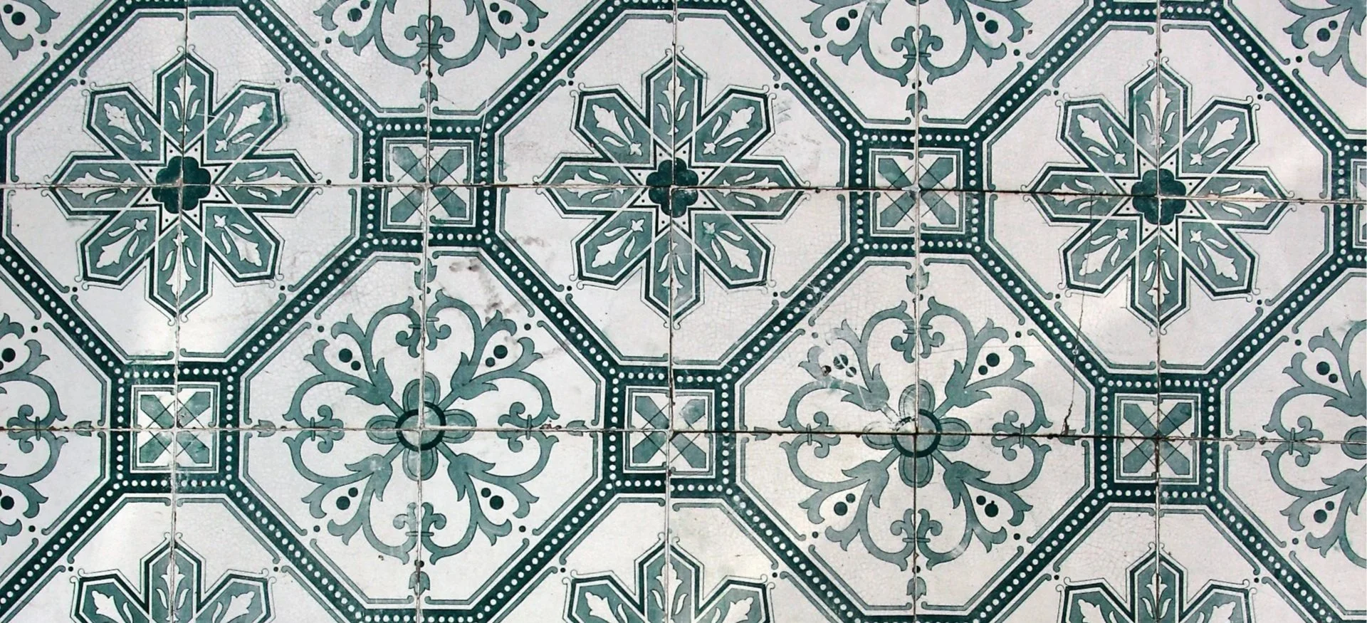 A top-down view of traditional Portuguese azulejo tiles featuring a repeating geometric and floral pattern in teal and white.