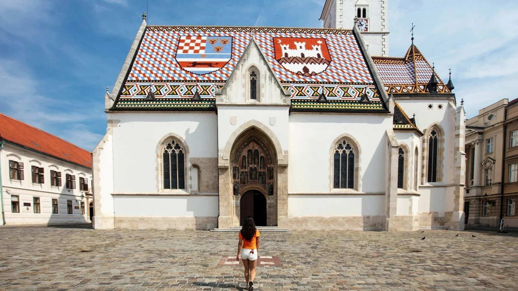 A woman walks toward St. Mark's Church in Zagreb, Croatia, famous for its colorful tiled roof depicting the medieval coats of arms of Croatia, Dalmatia, and Slavonia.