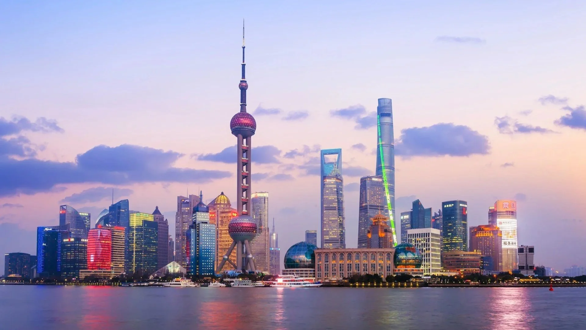 The Shanghai skyline at twilight featuring the Oriental Pearl Tower and surrounding skyscrapers reflected on the water.