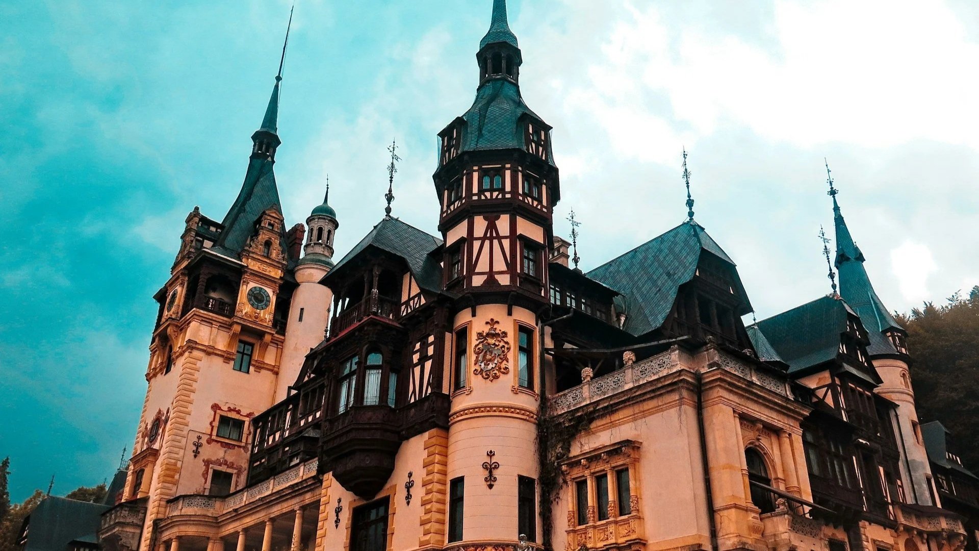 The ornate, multi-turreted Neo-Renaissance facade of Peleș Castle in Sinaia against a dramatic sky.