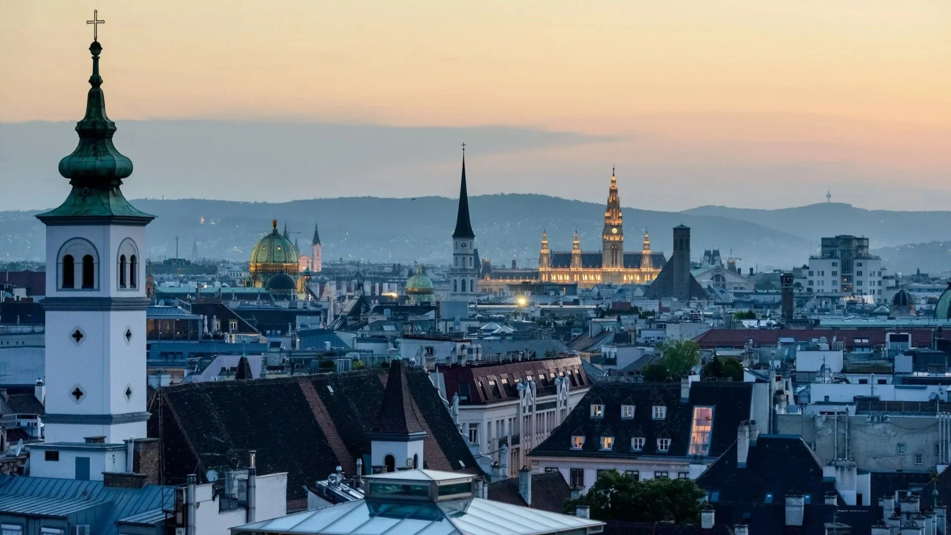 Panoramic sunset view over the rooftops, church spires, and historical architecture of Vienna.