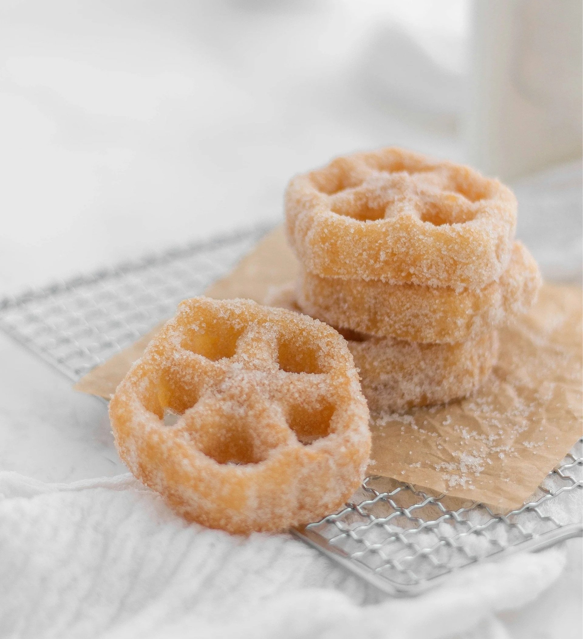 A stack of flower-shaped, sugar-coated buñuelos resting on a wire cooling rack.