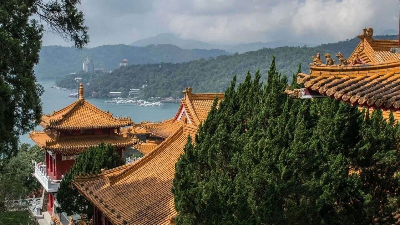 The intricate, golden-yellow tiled roofs of a traditional Taiwanese temple overlooking a wide blue lake surrounded by misty hills.