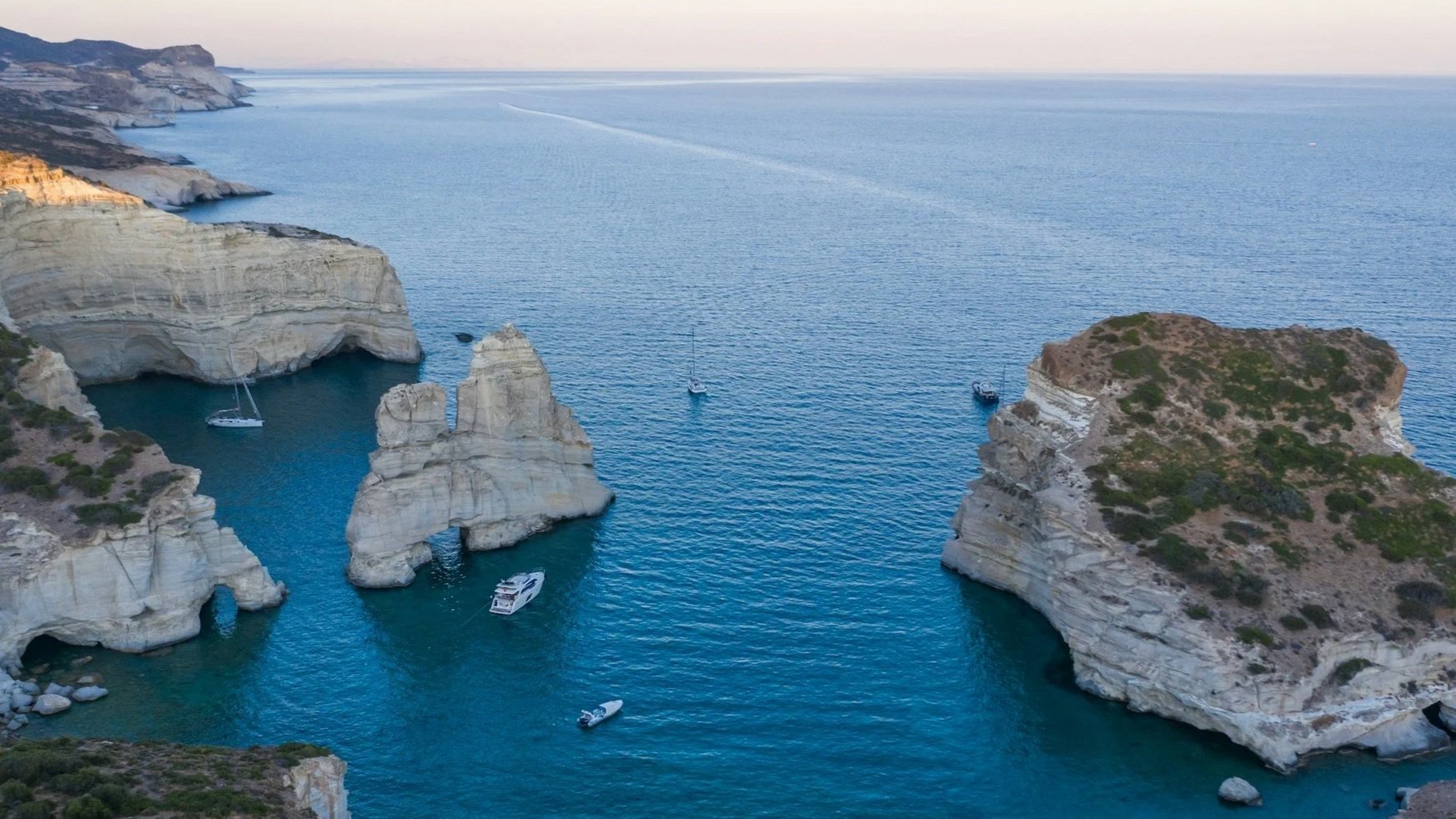 Aerial view of dramatic white volcanic rock formations and turquoise water off the coast of Milos, Greece.