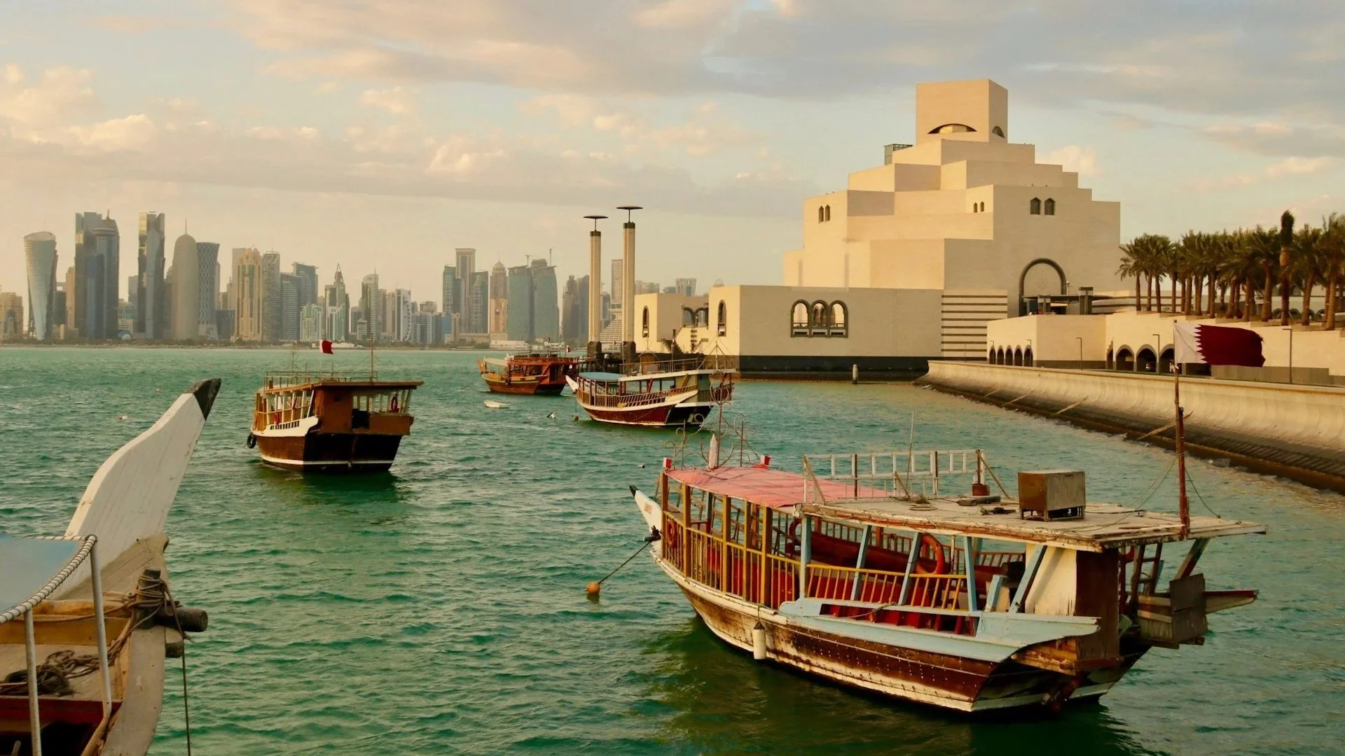 Traditional Qatari dhow boats anchored in Doha harbor near the Museum of Islamic Art with the city skyline behind them.