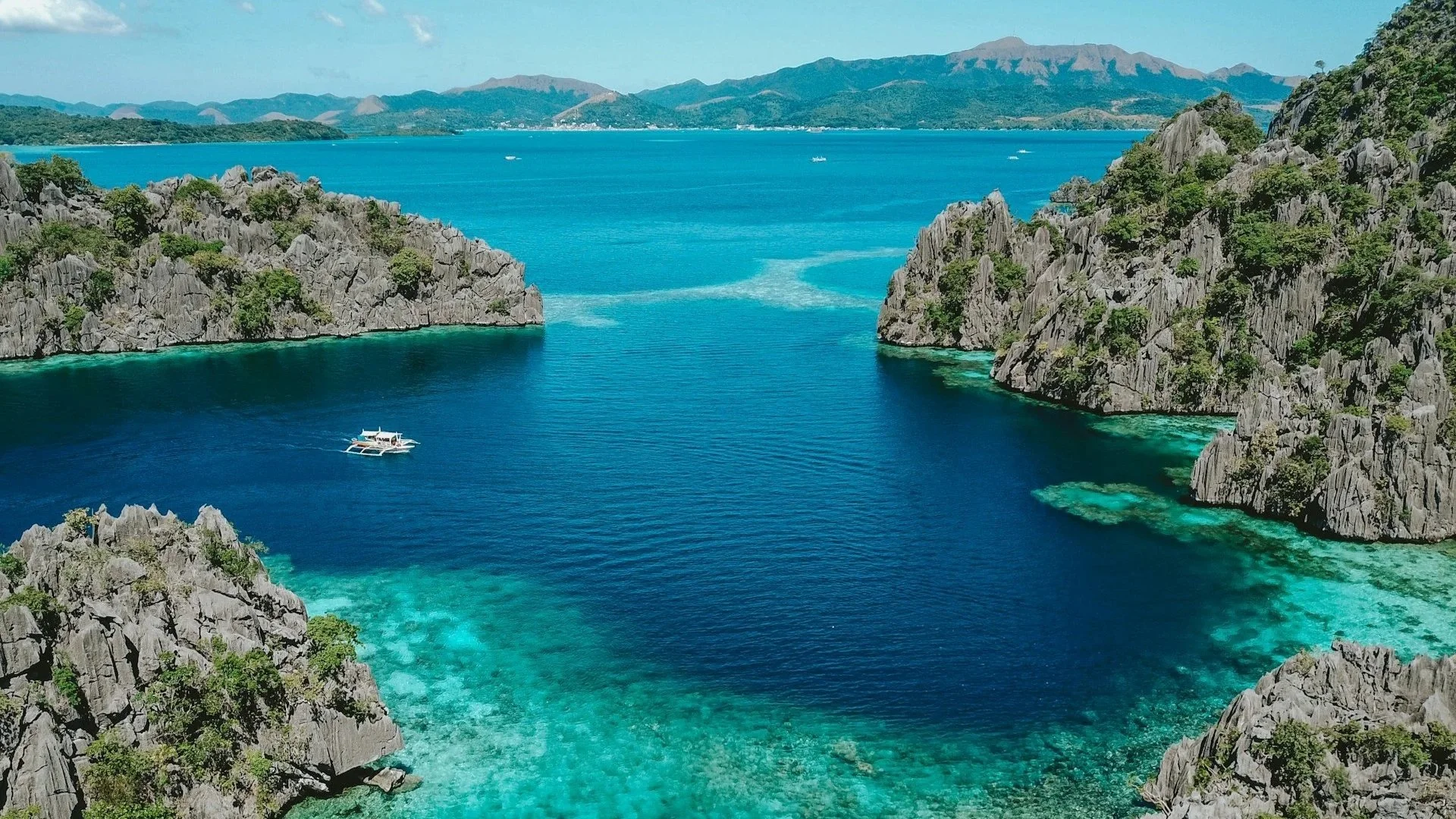 High-angle view of a deep blue sea surrounded by dramatic, rocky limestone cliffs and bright turquoise coral reefs.