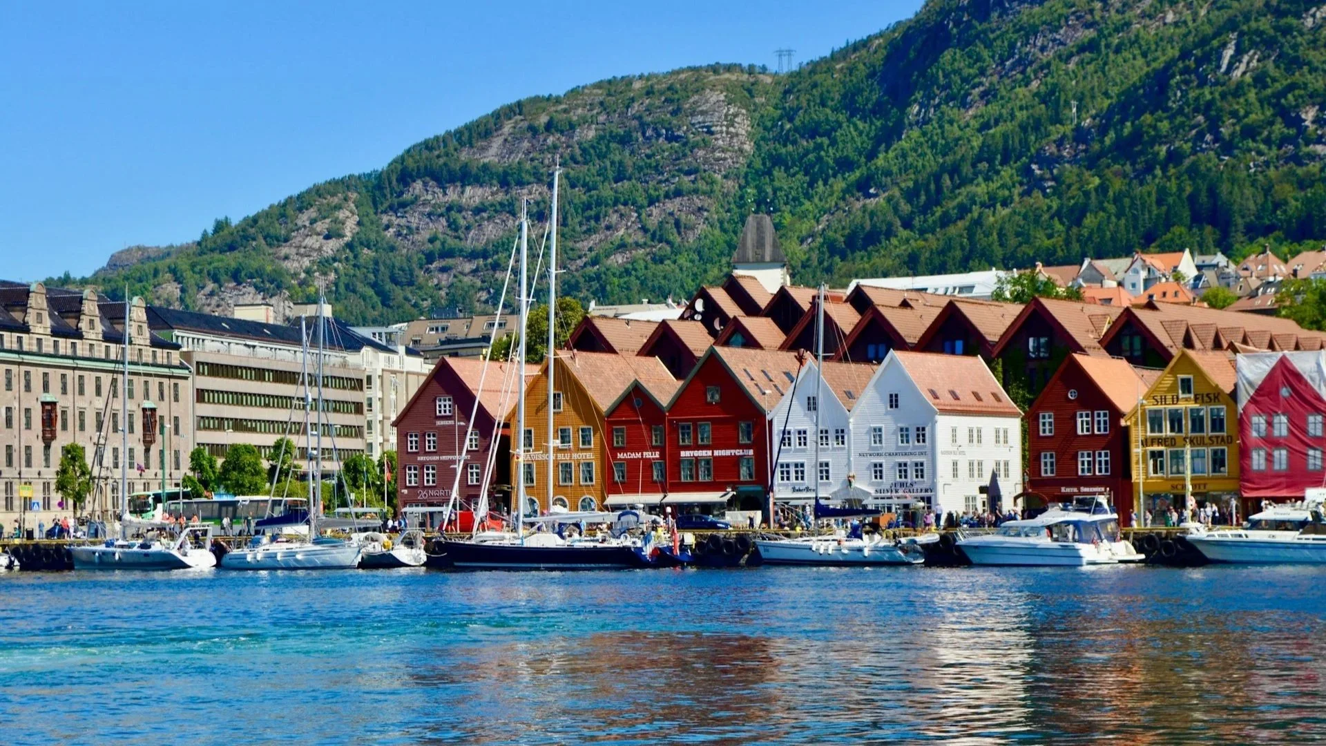 Red and white traditional fishing huts on stilts over calm water, set against a backdrop of misty, rugged mountains.