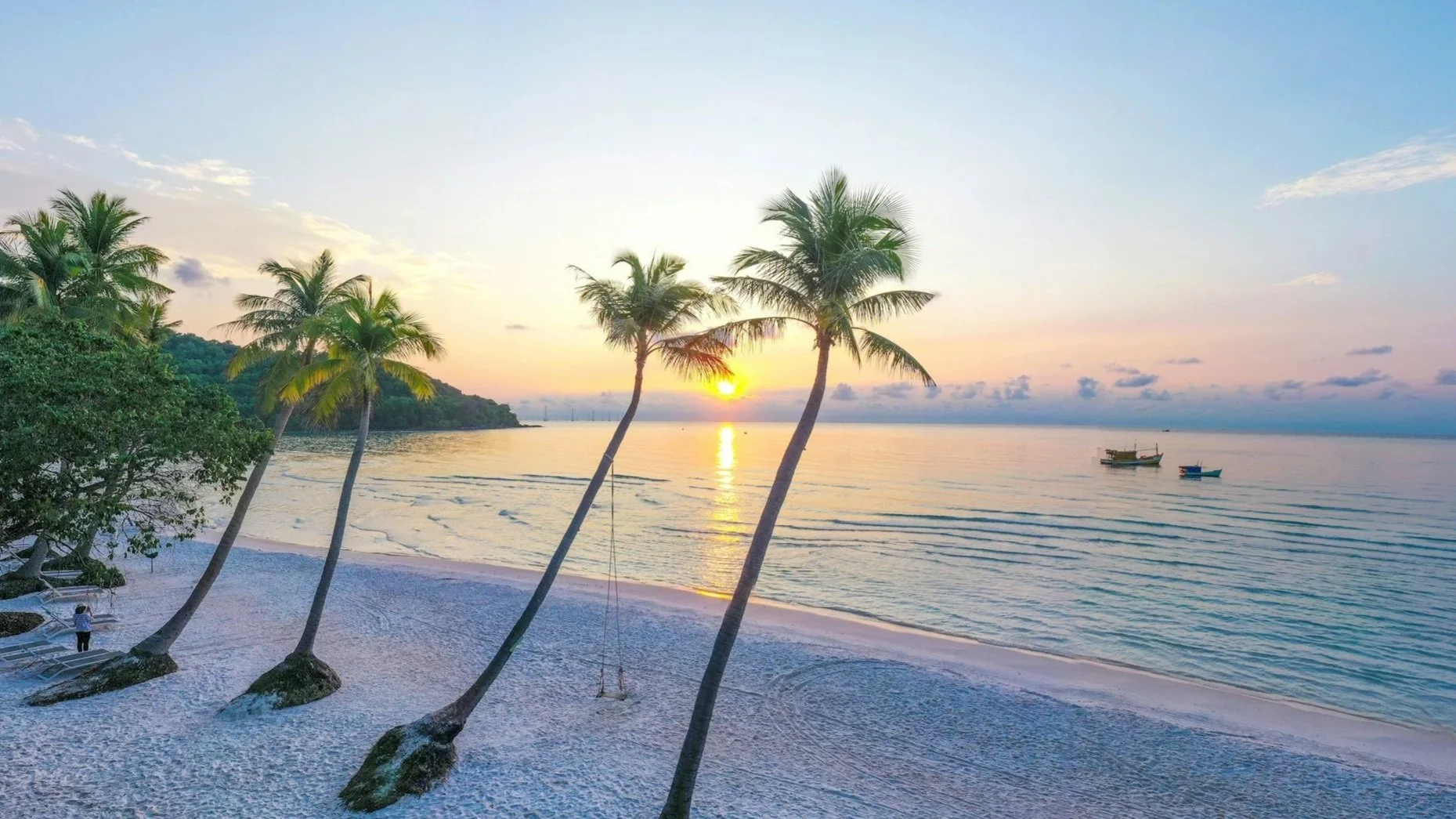 A serene tropical beach at sunset with leaning palm trees and white sand.