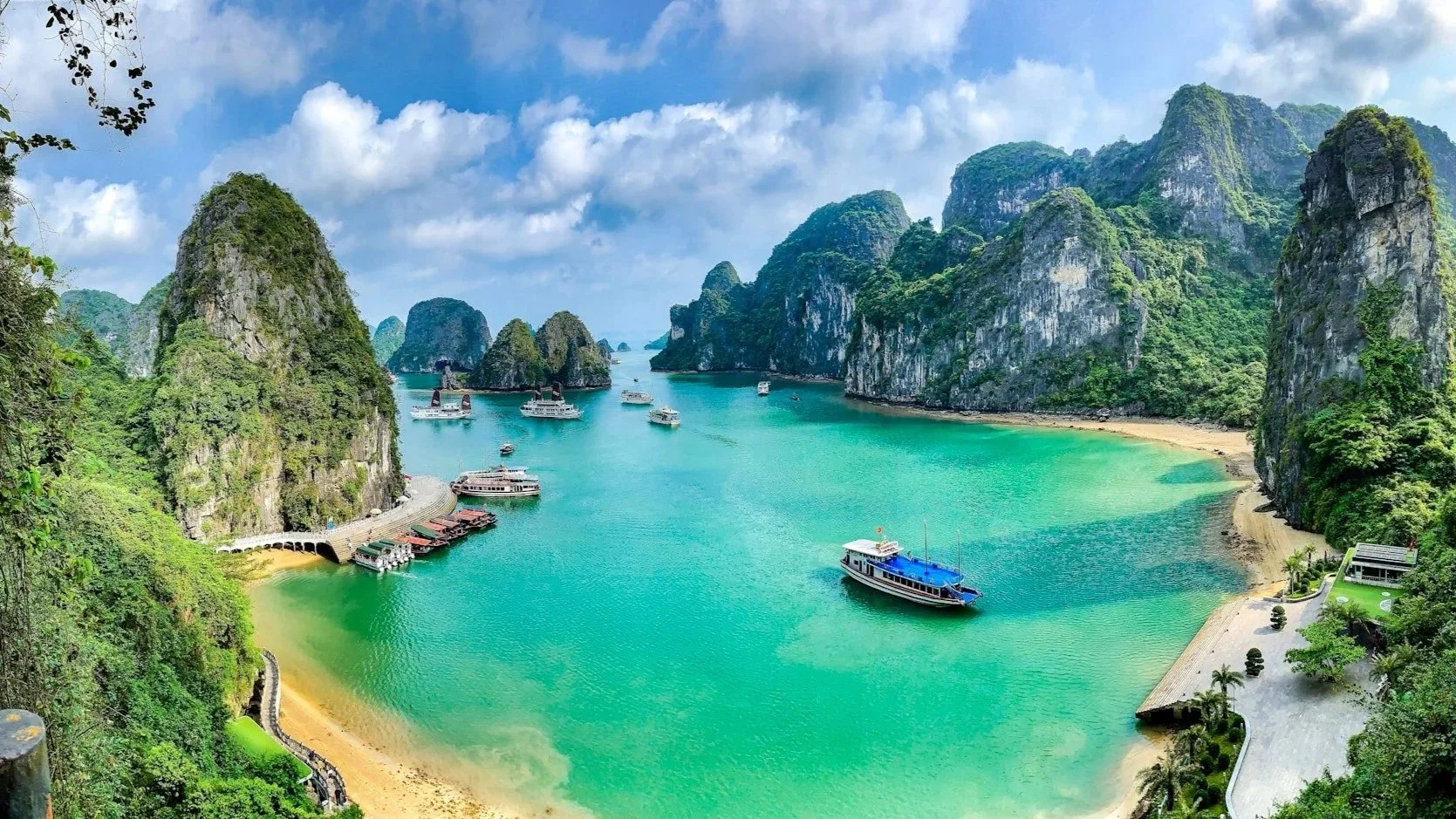 A panoramic view of Ha Long Bay featuring limestone karsts, emerald water, and tour boats.
