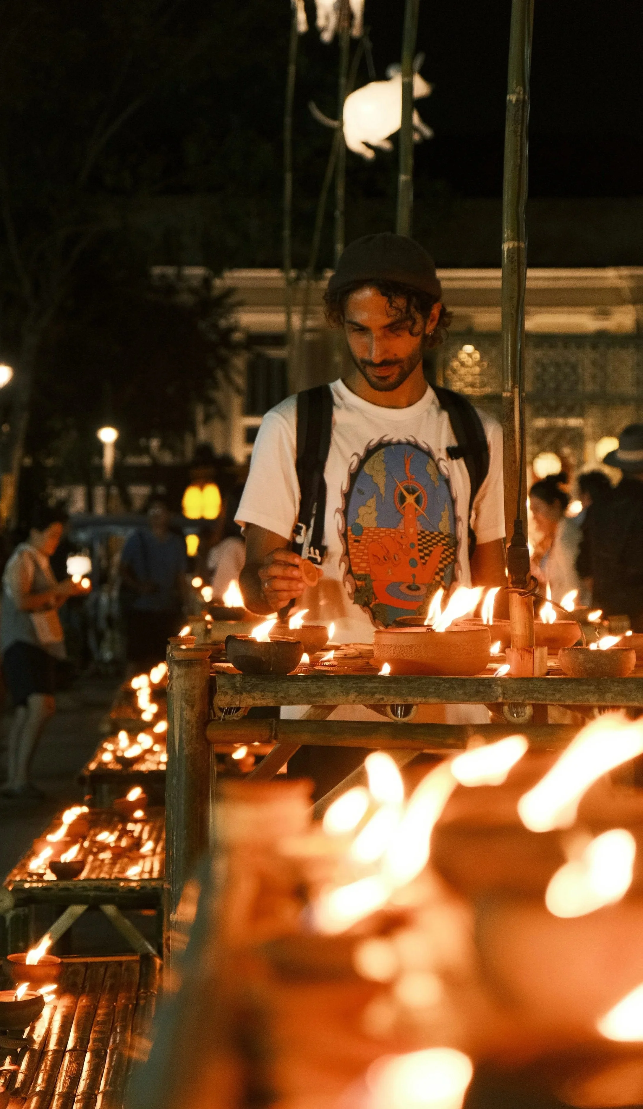 Man lighting small clay oil lamps at a **night festival** in Thailand.