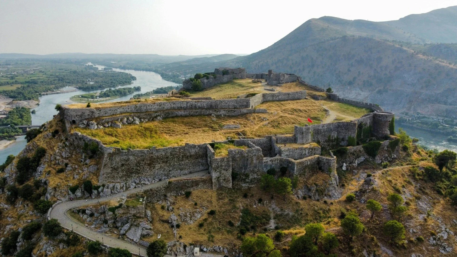 Aerial view of an ancient stone fortress sitting atop a hilltop overlooking a winding river and valley.