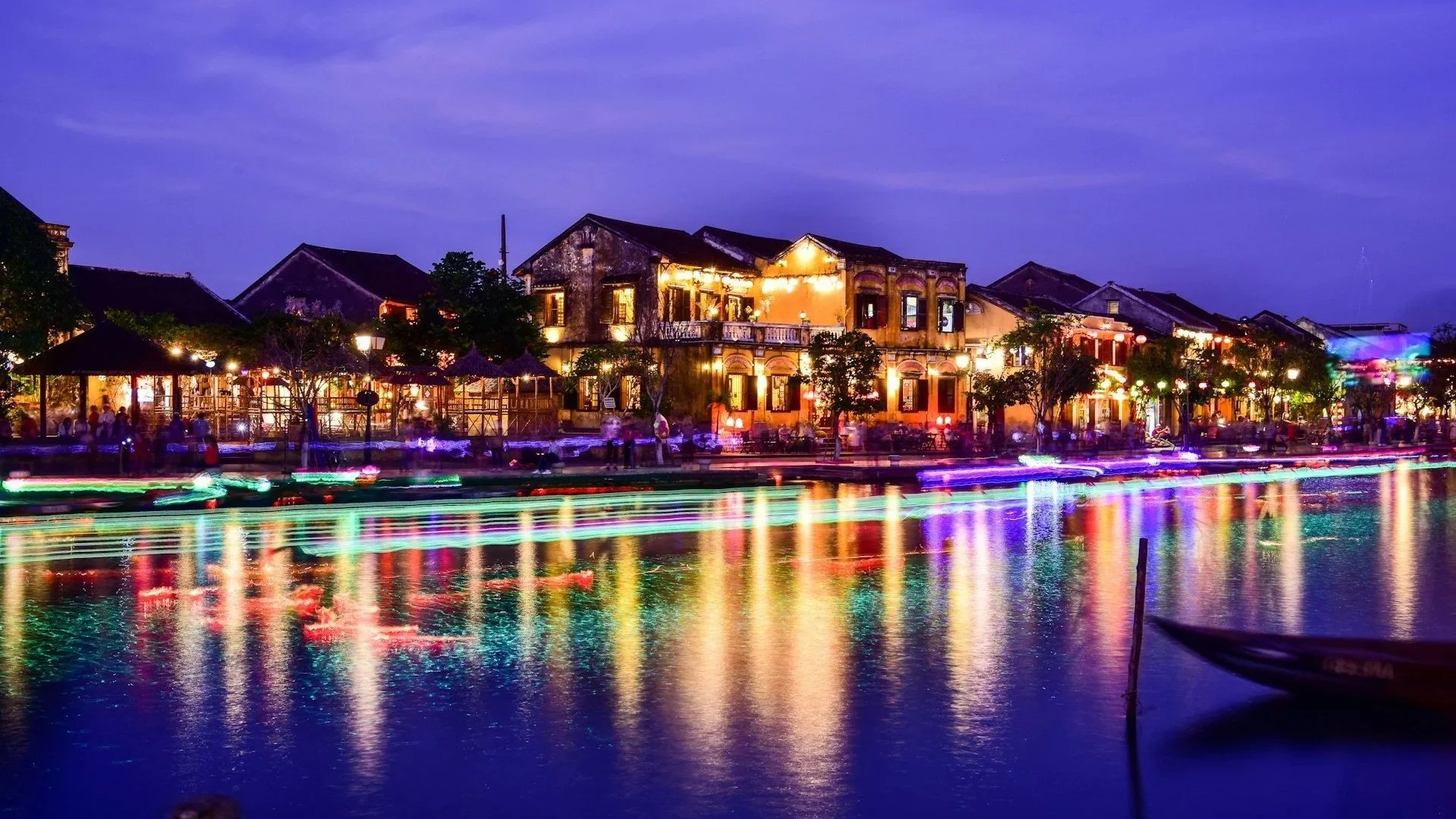 Vibrant night view of Hoi An’s ancient town with glowing lanterns reflecting on the river water.
