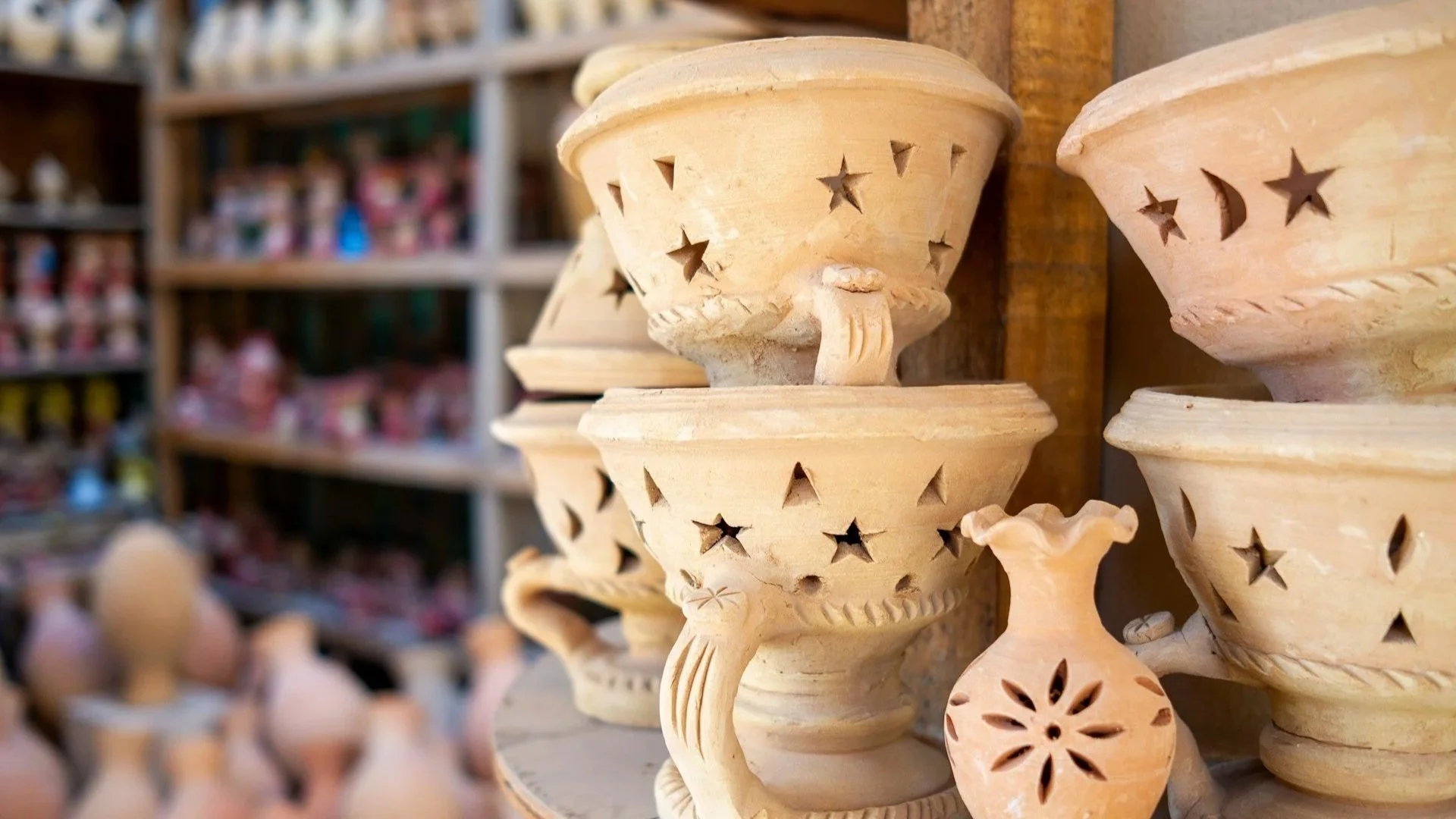 A close-up of stacked, hand-carved clay incense burners and pottery sitting on a wooden table in a market.