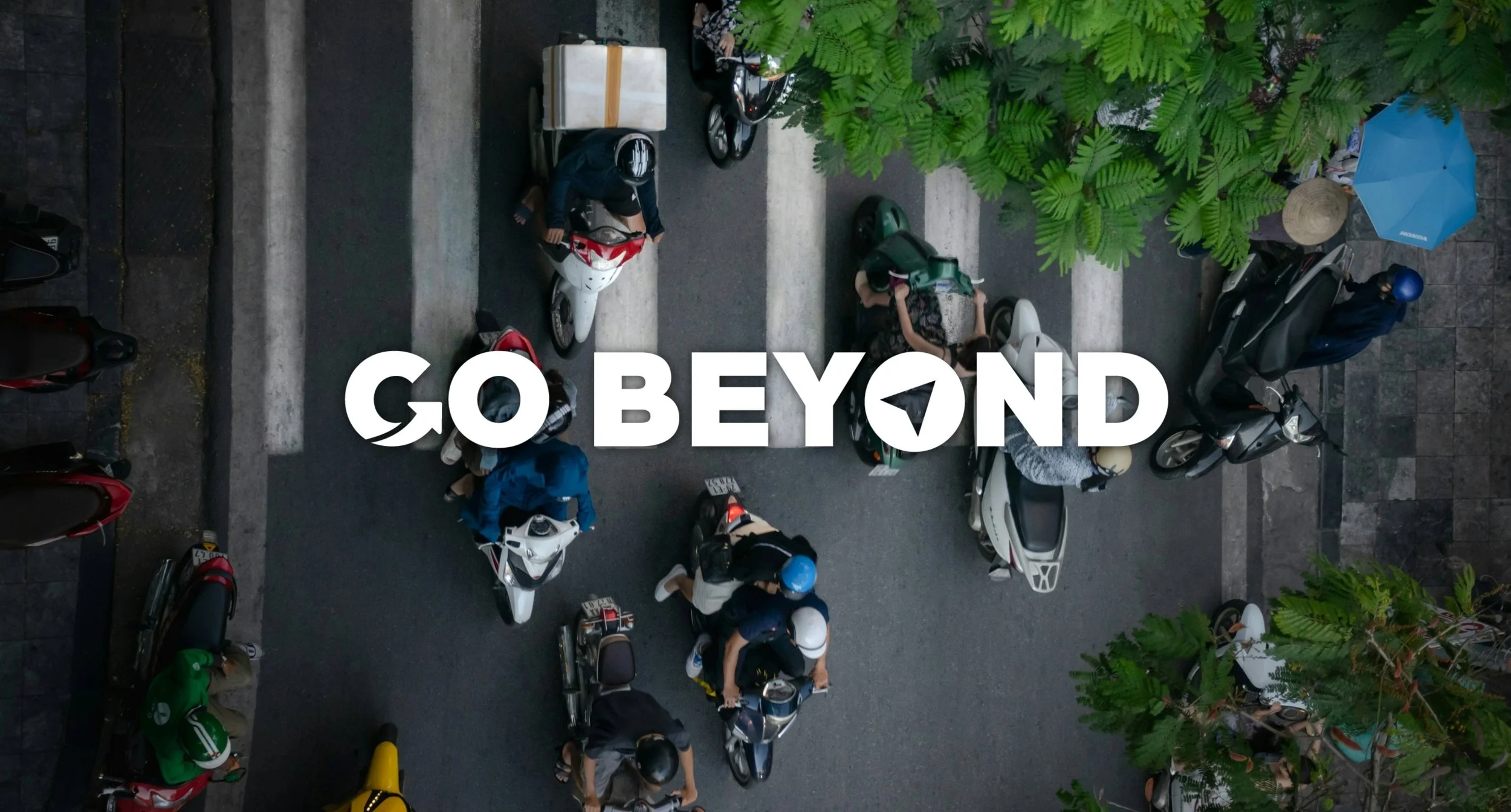 An aerial view of motorbikes crossing a white-striped pedestrian walk in Vietnam, with the text "GO BEYOND" overlaid in white.
