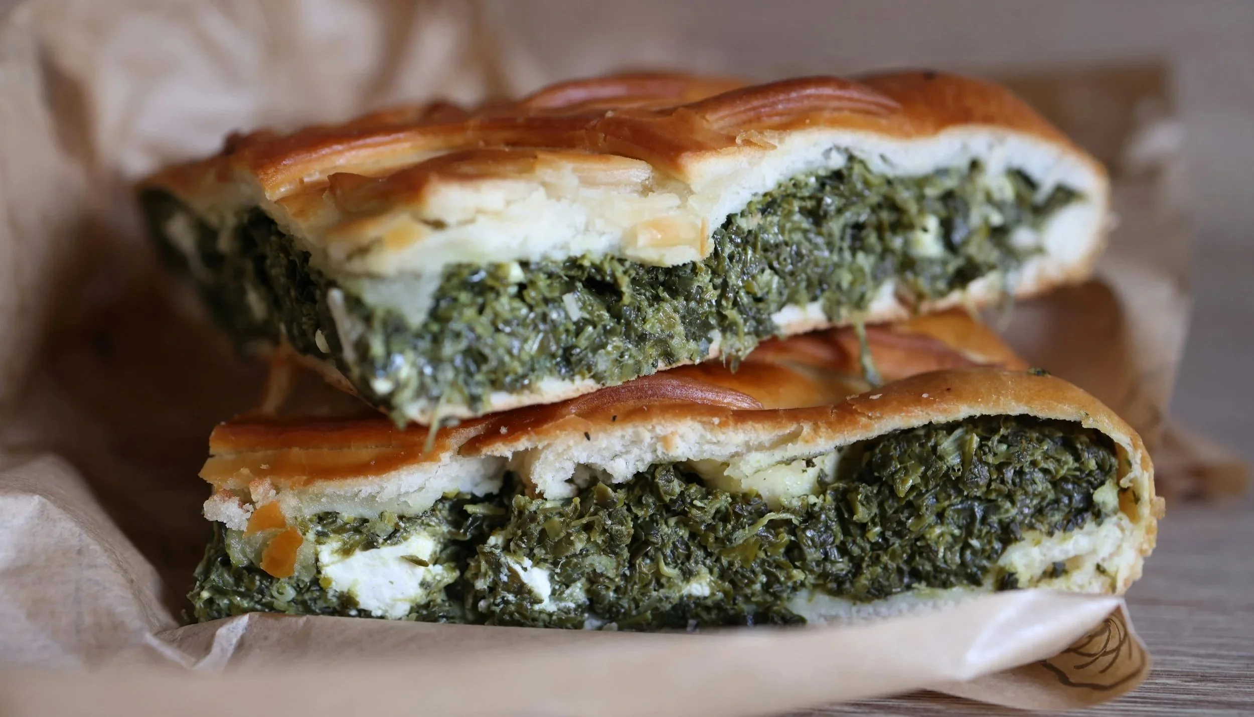 Close-up of two pieces of a savory spinach and cheese pie (Spanakopita) on paper.