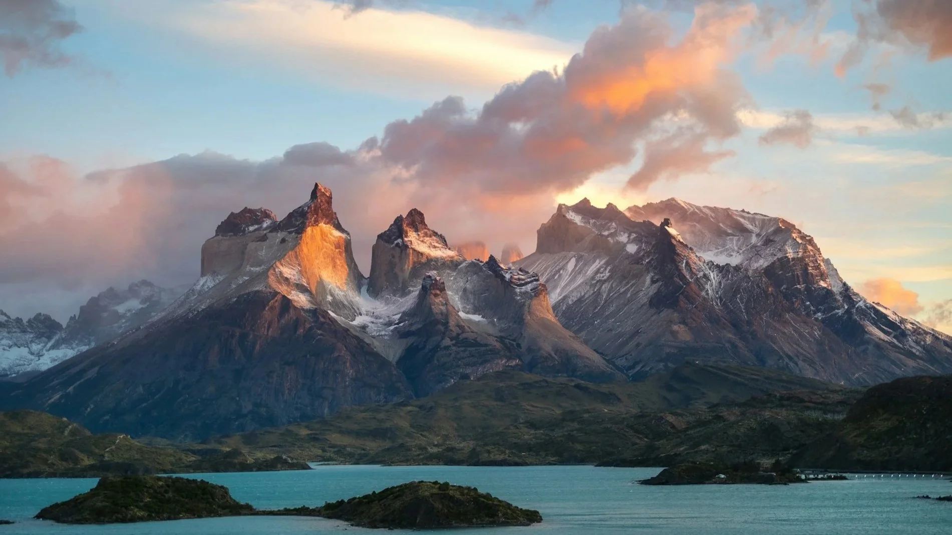 Jagged mountain peaks of Torres del Paine glowing orange at sunset over a turquoise lake.