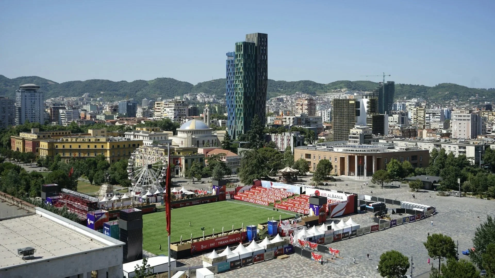High-angle cityscape featuring a public square, modern skyscrapers, and a temporary outdoor sports event.