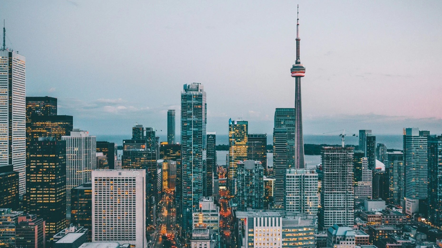 An aerial view of the Toronto city skyline at dusk, featuring the CN Tower and illuminated skyscrapers.