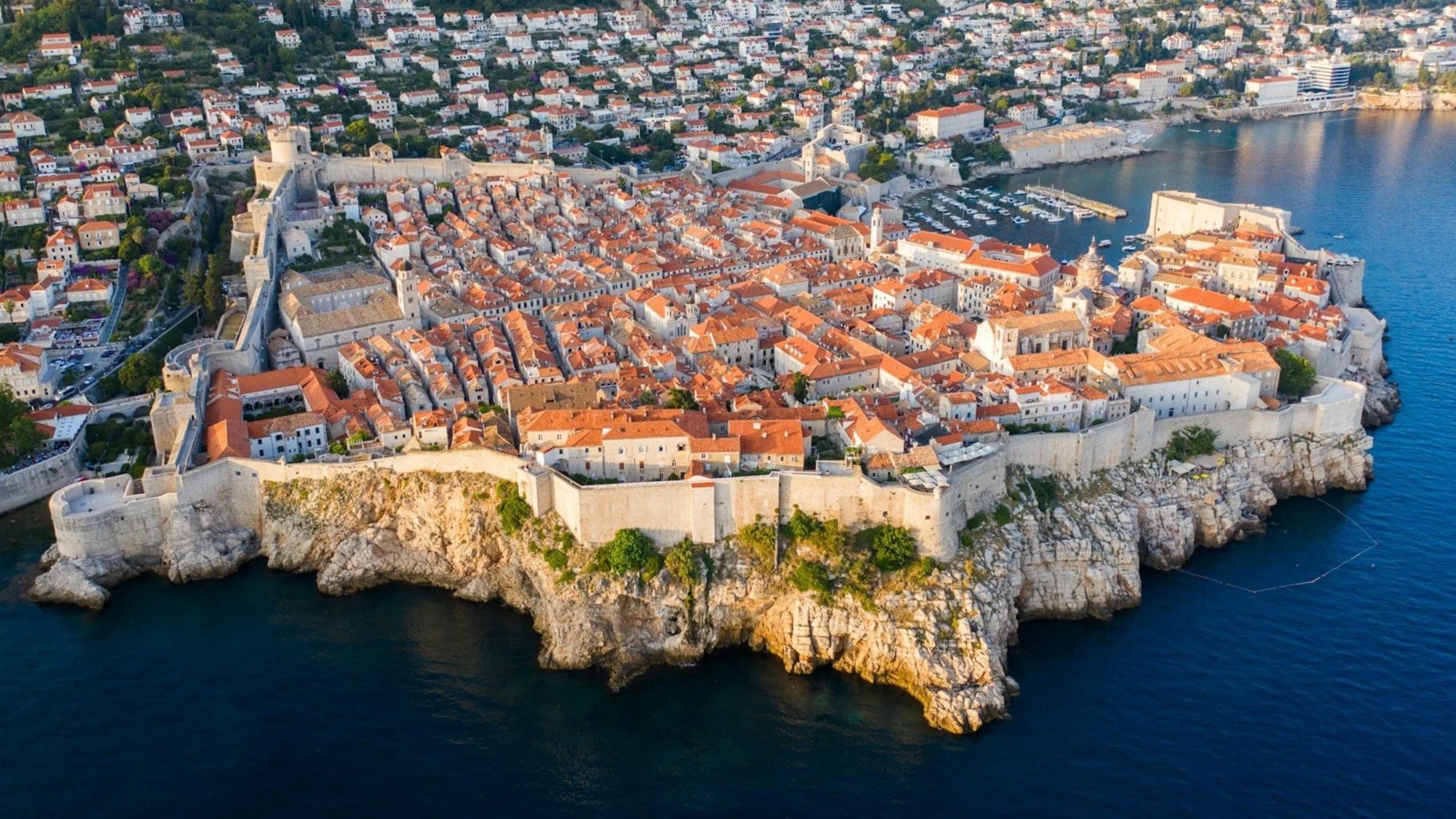 Aerial view of the historic Old Town of Dubrovnik, showing its stone walls and terracotta rooftops jutting into the Adriatic Sea.