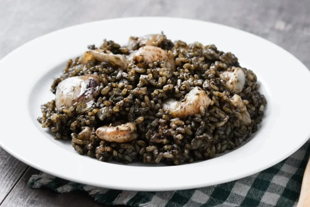 A traditional Croatian fish stew (Gregada) in a ceramic dish, featuring thick fillets of white fish, sliced potatoes, onions, cherry tomatoes, and lemon slices in a light broth.