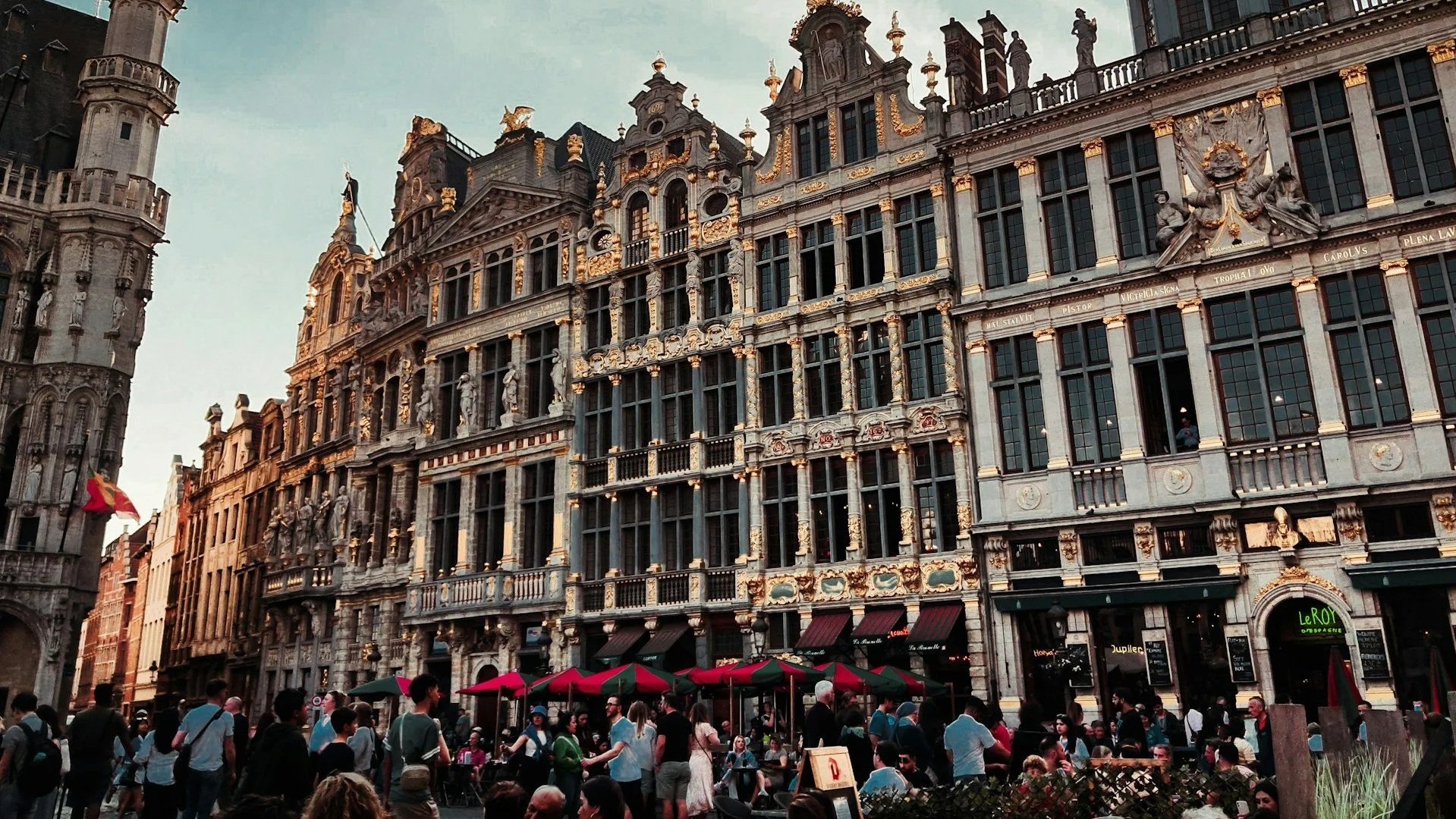 Busy Grand-Place square in Brussels featuring historic guildhouses with gold accents and outdoor dining cafes.