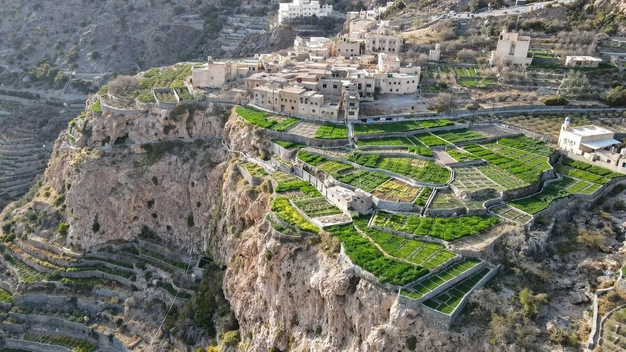 A traditional stone village perched on a steep cliffside, surrounded by vibrant green terraced farms.