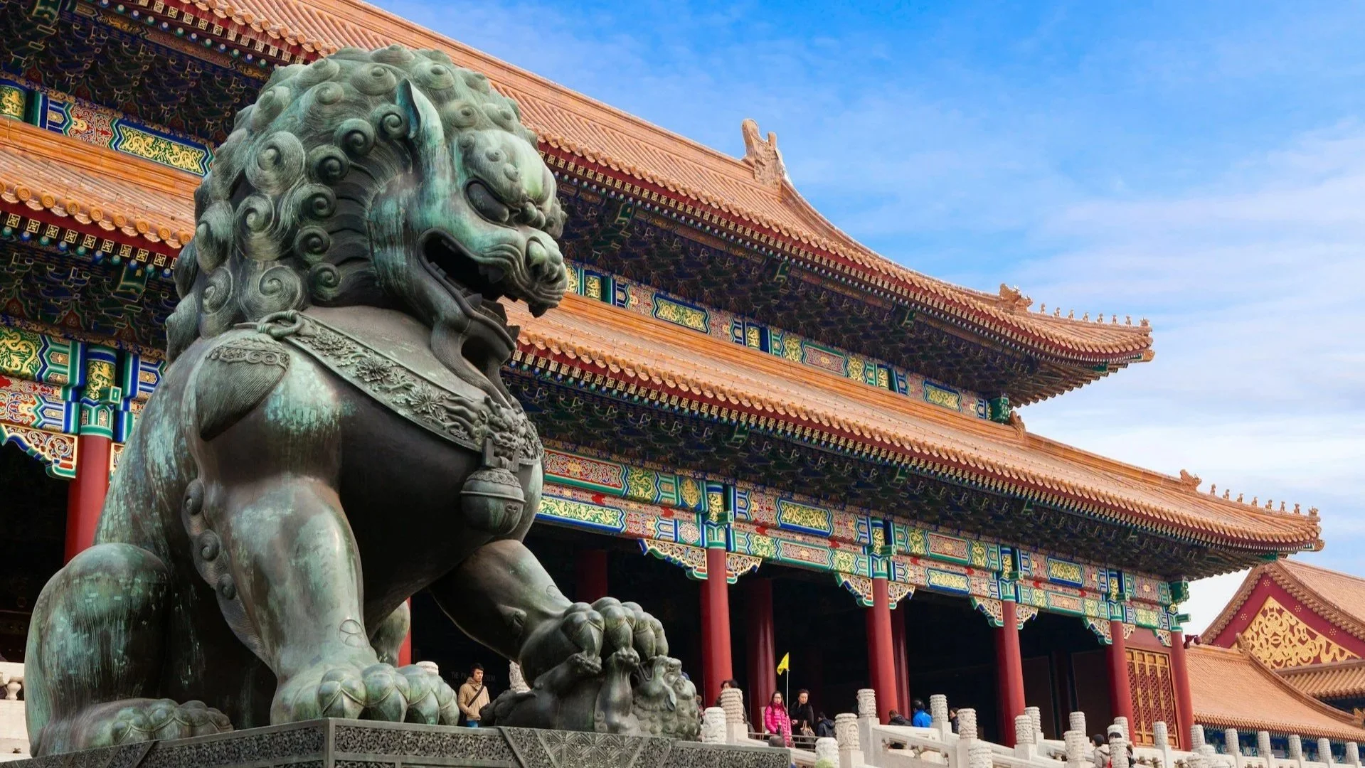 Large bronze guardian lion statue in front of a traditional Chinese temple building with intricate painted eaves.