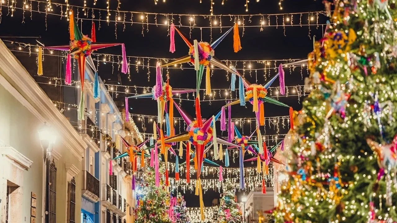 A street at night decorated with colorful star-shaped piñatas and hanging string lights.