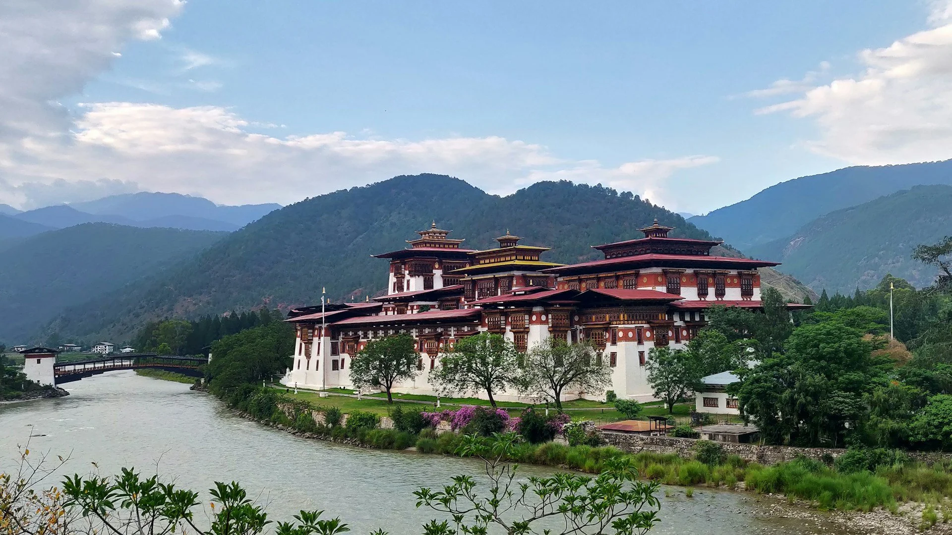 Punakha Dzong, a majestic Tibetan-style fortress and monastery with white walls and ornate red roofs, sits at the junction of two rivers in a lush valley beneath rolling green mountains in Bhutan.