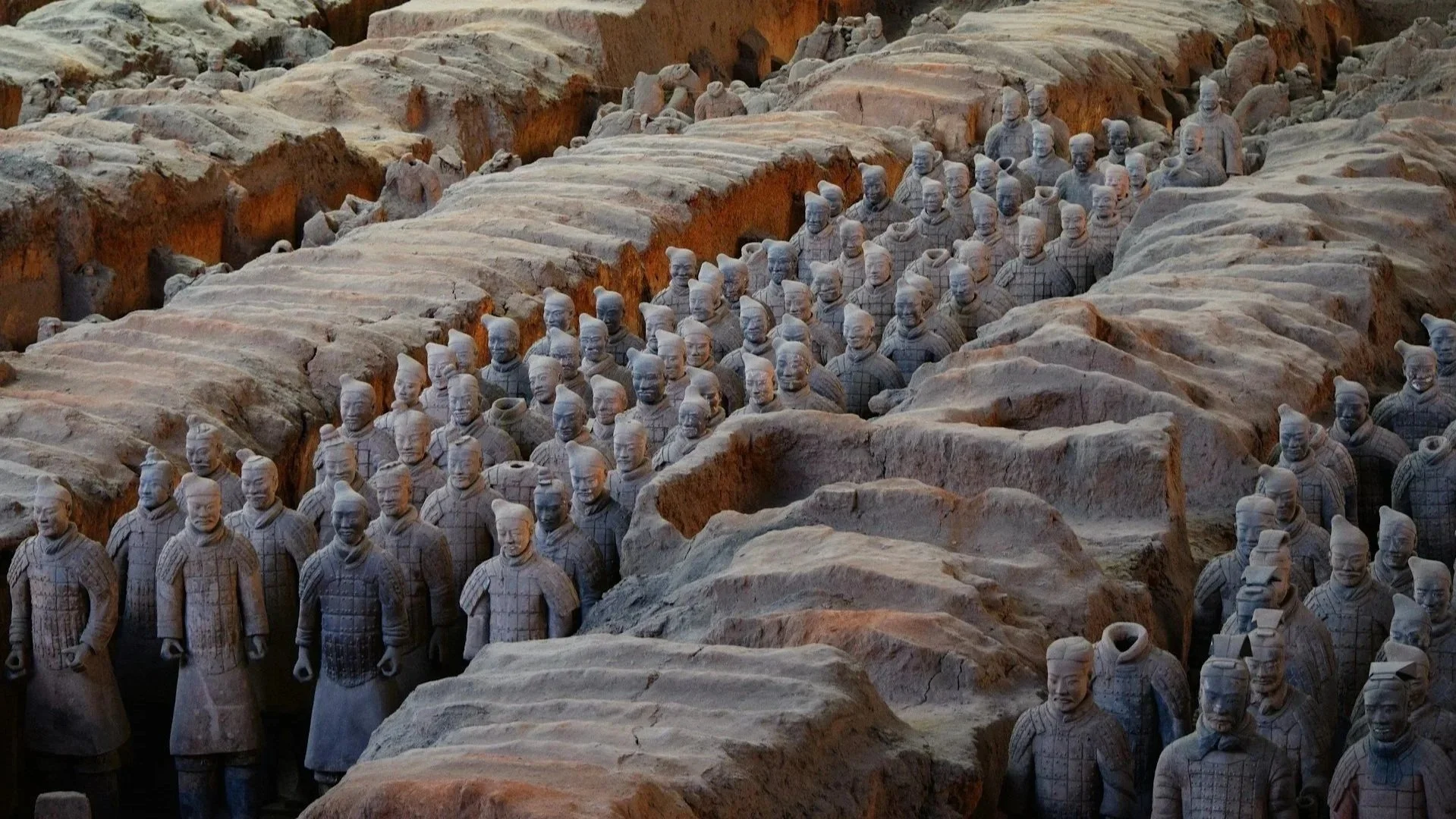 High-angle view of life-sized terracotta warrior statues standing in archaeological excavation pits.