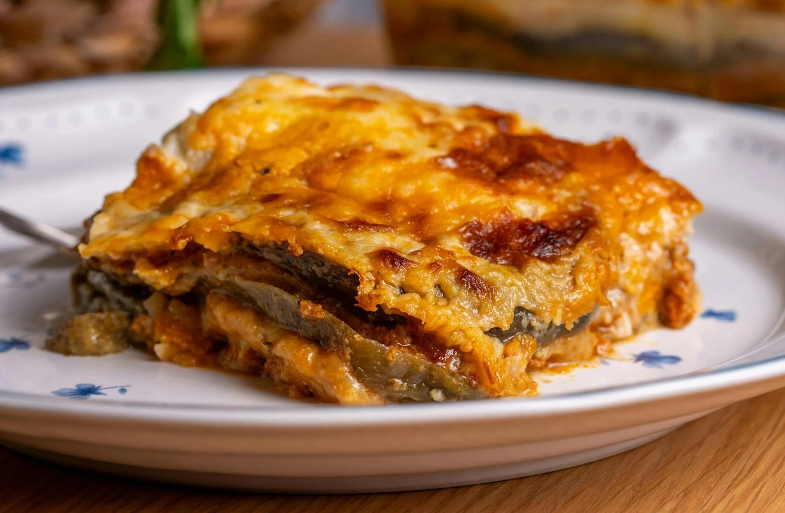 A slice of baked Moussaka or lasagna with layers of eggplant and cheese on a white plate.
