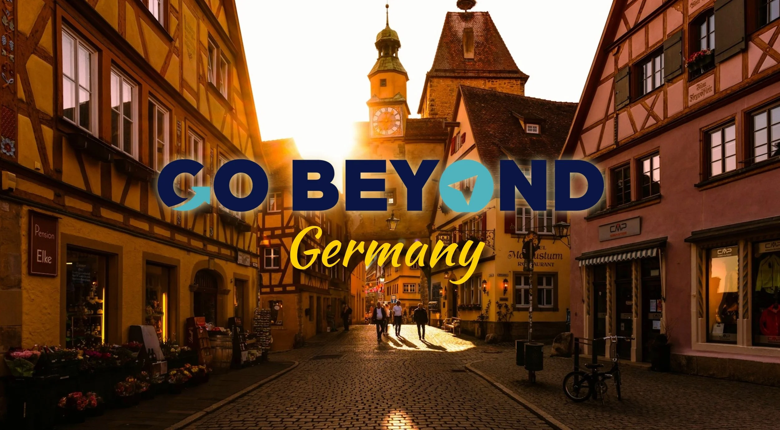 Graphic overlay reading "GO BEYOND Germany" centered over a warm, sunlit photo of a historic, narrow cobblestone street in Rothenburg ob der Tauber, lined with traditional half-timbered buildings.