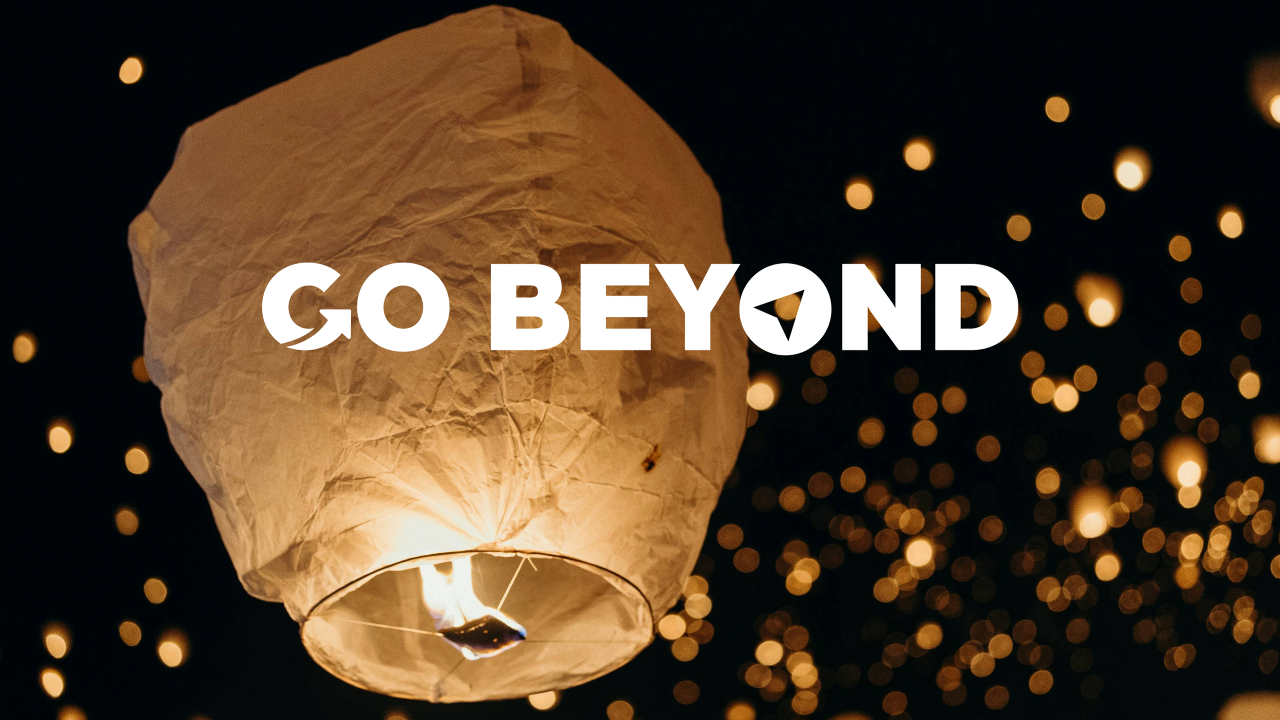White sky lantern floating into the night sky among many glowing lights, with the text "GO BEYOND" overlaid.
