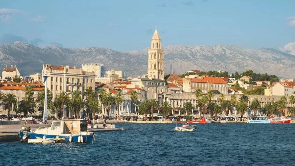 The Split waterfront (Riva) showing the Cathedral of Saint Domnius bell tower against a mountain backdrop.