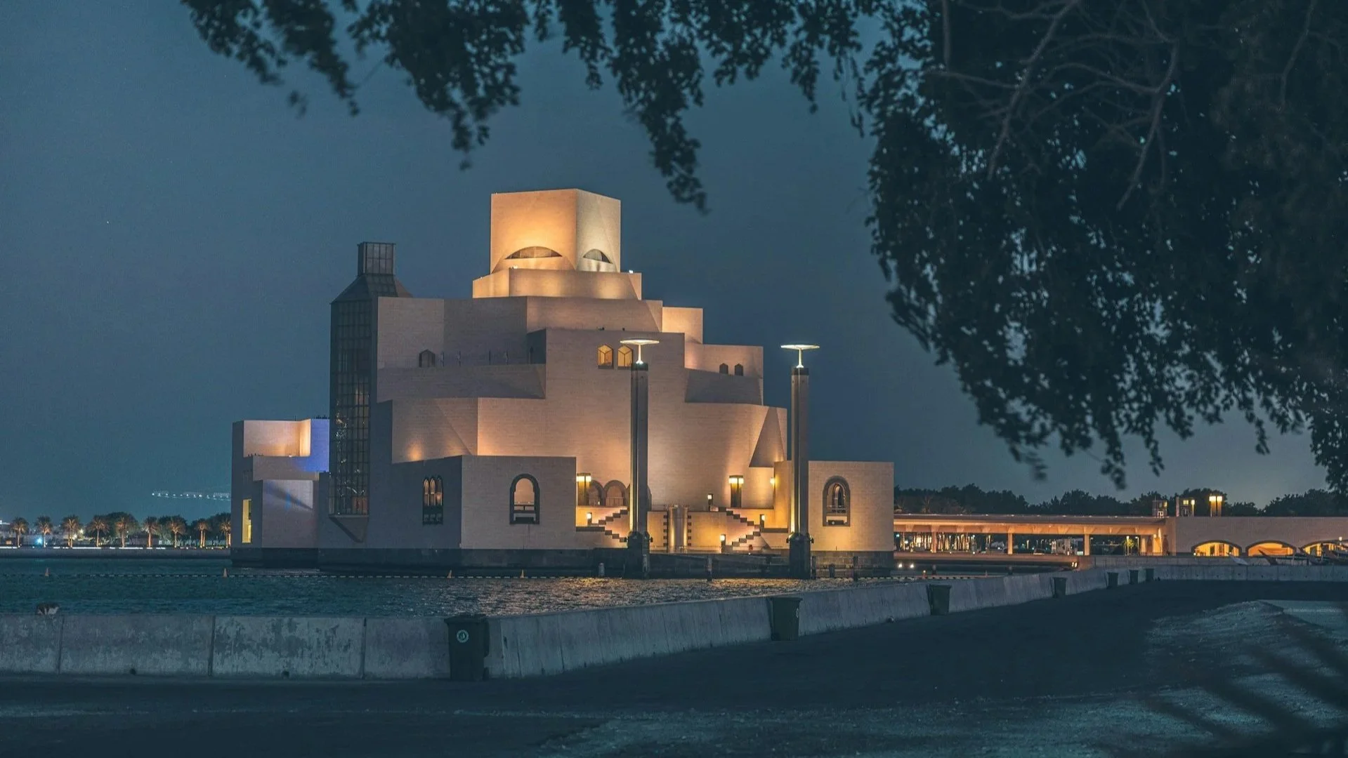 The geometric, tiered exterior of the Museum of Islamic Art illuminated at night along the Doha waterfront.