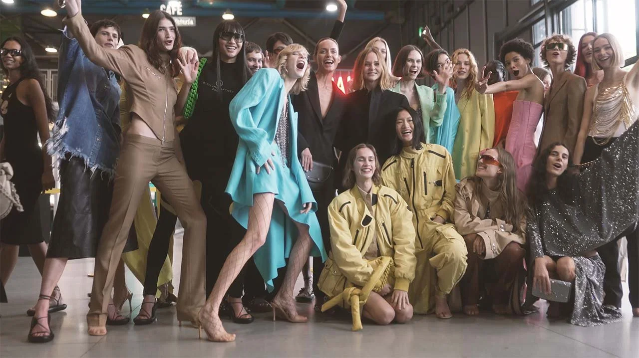 Group of women and girls dressed in colorful fashion, smiling and posing together indoors.