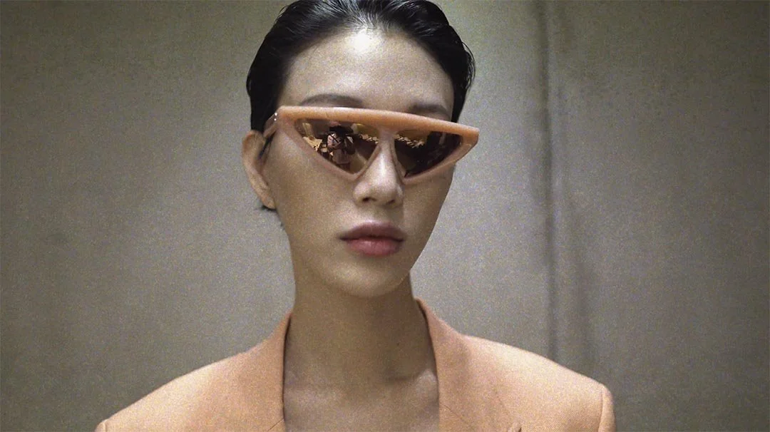 A woman with short dark hair wearing peach-colored sunglasses and a matching peach blazer.