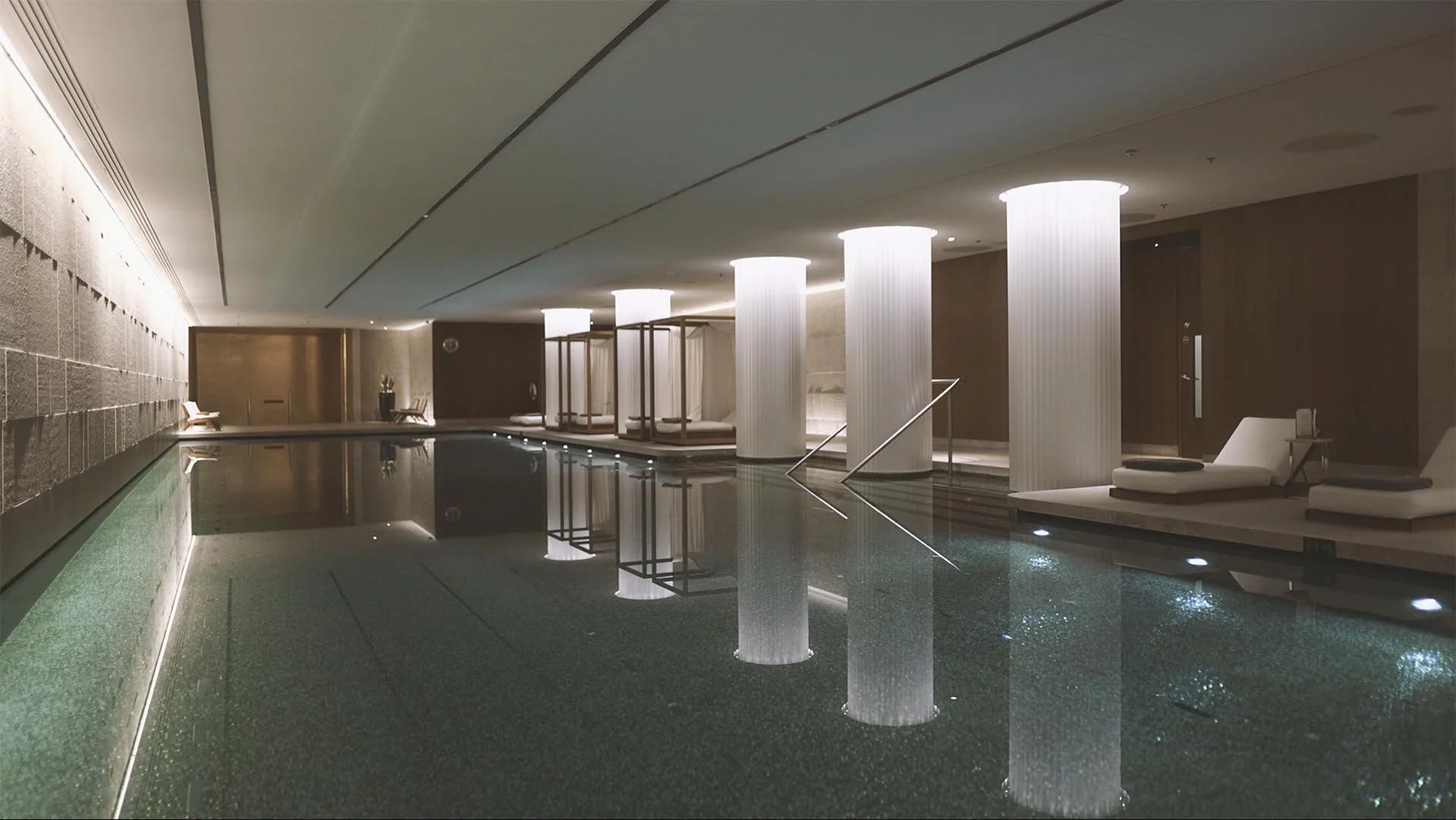 Bvlgari indoor pool area with white illuminated columns, lounge chairs, and a reflective water surface.